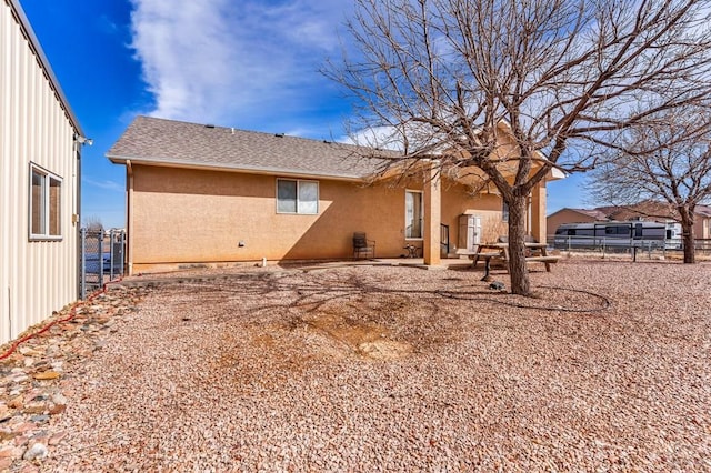 rear view of property featuring a shingled roof, fence, and stucco siding