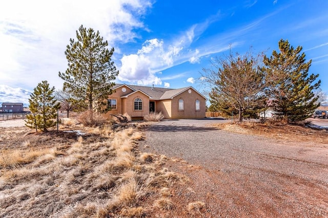 view of front facade with gravel driveway, fence, and stucco siding