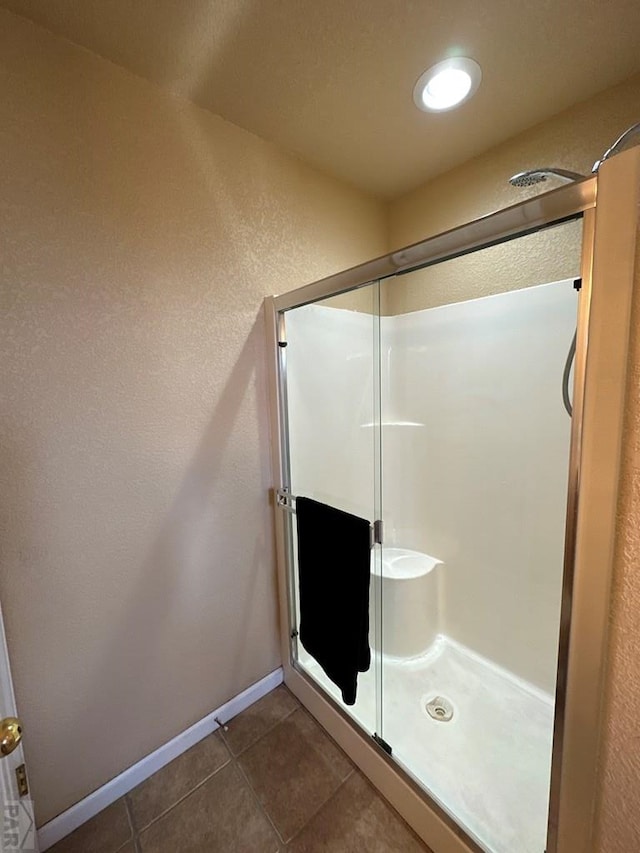 full bath with a textured wall, a shower stall, baseboards, and tile patterned floors