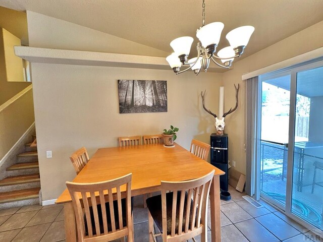 dining room featuring lofted ceiling, light tile patterned floors, baseboards, stairs, and an inviting chandelier