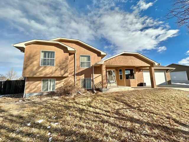 rear view of house with central air condition unit, stucco siding, concrete driveway, an attached garage, and fence