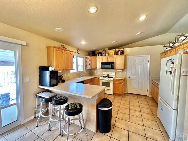 kitchen with a breakfast bar, light countertops, a sink, white appliances, and a peninsula