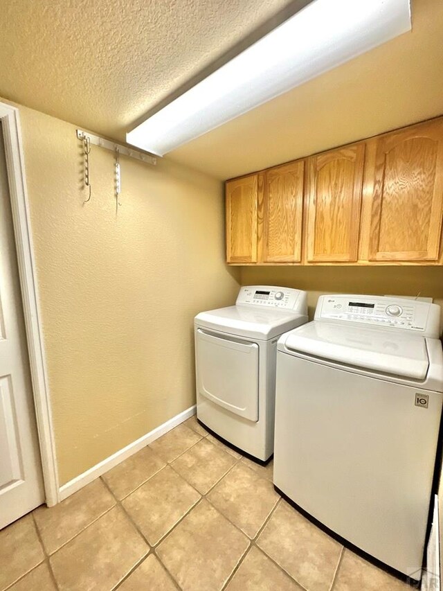 laundry area featuring a textured ceiling, light tile patterned floors, separate washer and dryer, baseboards, and cabinet space