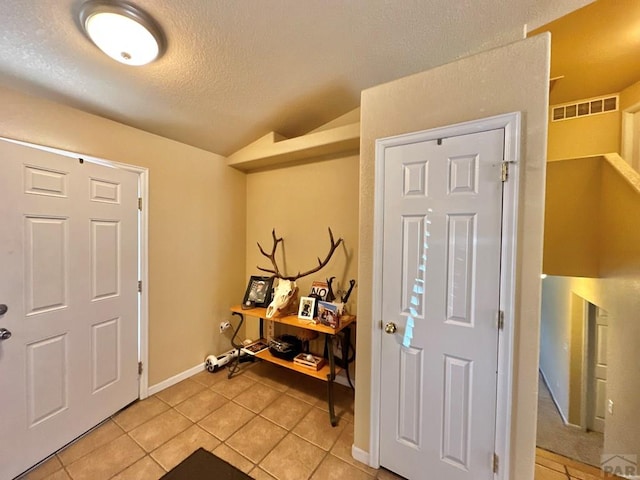 entrance foyer with light tile patterned floors, a textured ceiling, visible vents, baseboards, and vaulted ceiling