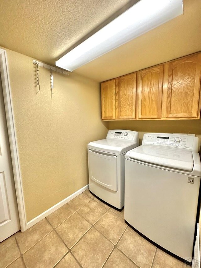 clothes washing area featuring washing machine and clothes dryer, light tile patterned floors, cabinet space, a textured ceiling, and baseboards