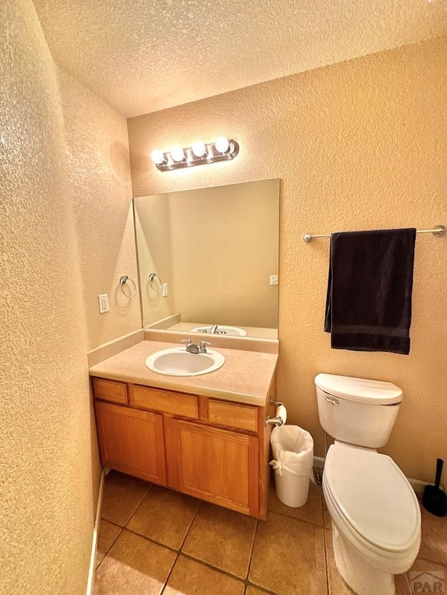 bathroom featuring a textured ceiling, a textured wall, tile patterned flooring, toilet, and vanity