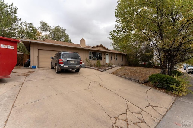 ranch-style home with a garage, concrete driveway, and a chimney