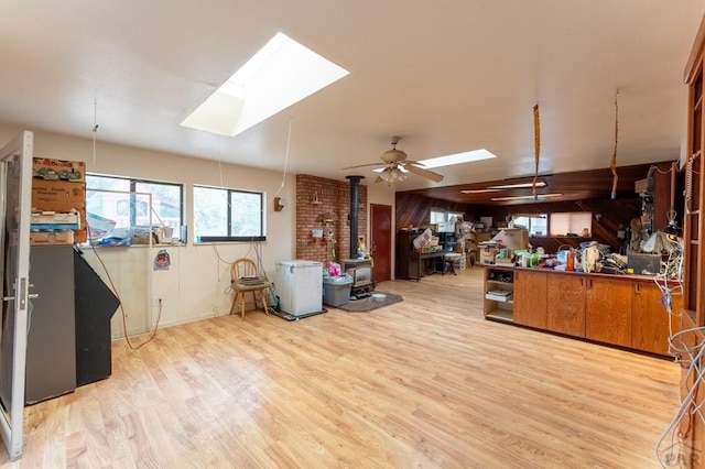 misc room featuring light wood-type flooring, a skylight, a wood stove, and a ceiling fan