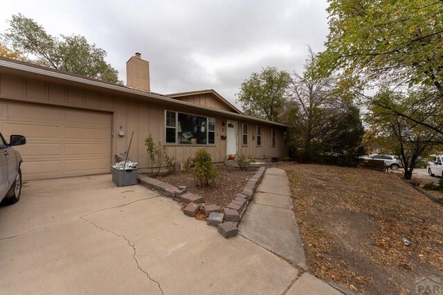 ranch-style home with a garage, concrete driveway, board and batten siding, and a chimney