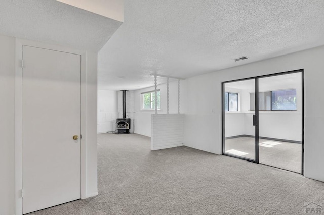 carpeted empty room with visible vents, a textured ceiling, and a wood stove