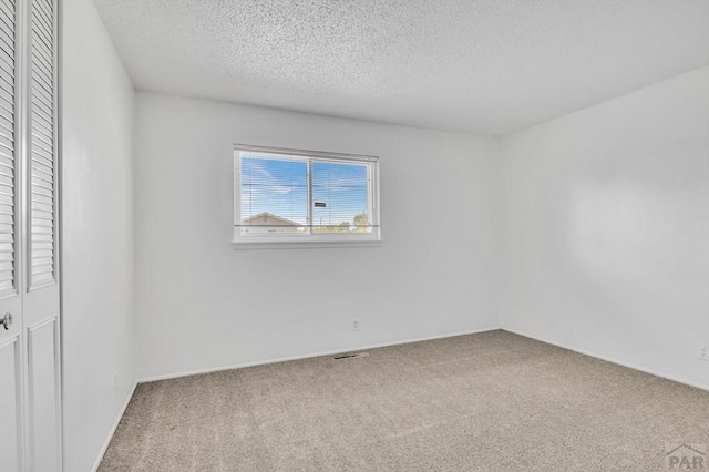 carpeted empty room with visible vents and a textured ceiling