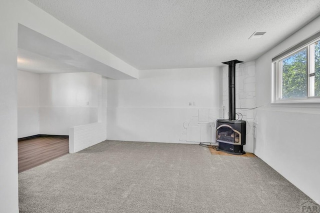 unfurnished living room featuring carpet flooring, a textured ceiling, a wood stove, and visible vents