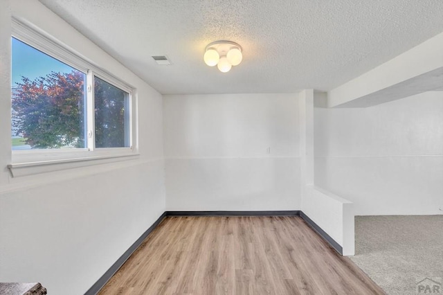 spare room with visible vents, a textured ceiling, baseboards, and wood finished floors