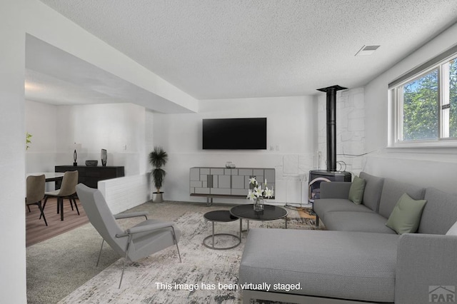 living area featuring visible vents, a textured ceiling, a wood stove, and wood finished floors