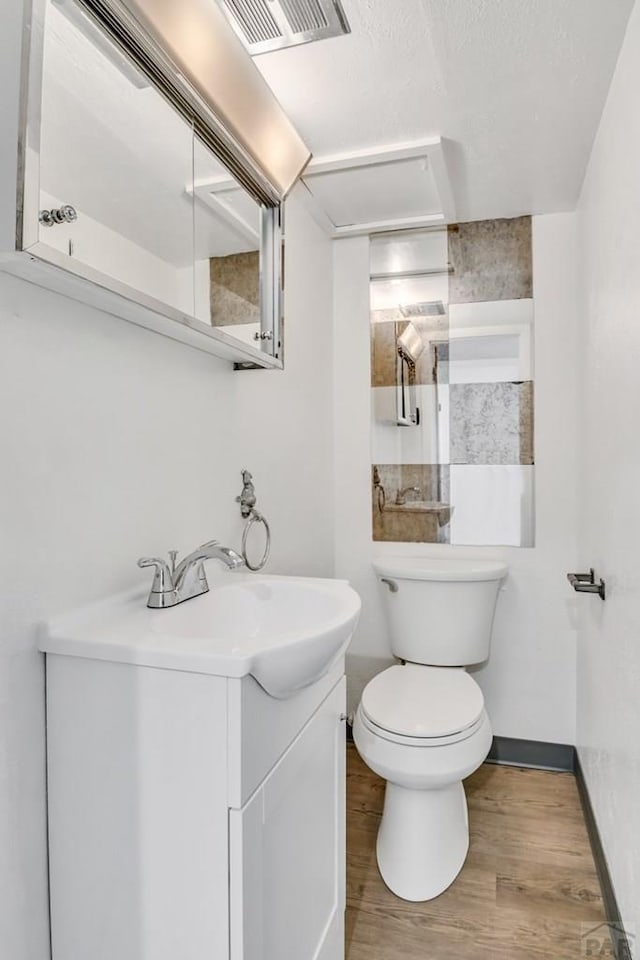 bathroom featuring visible vents, baseboards, toilet, wood finished floors, and vanity