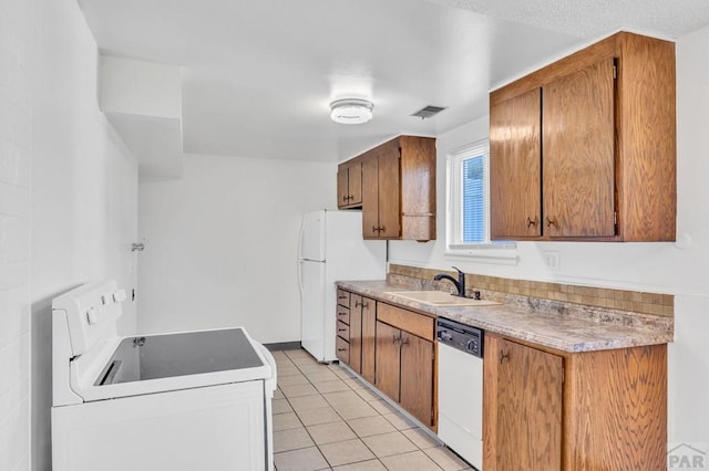 kitchen featuring brown cabinetry, light countertops, light tile patterned flooring, white appliances, and a sink