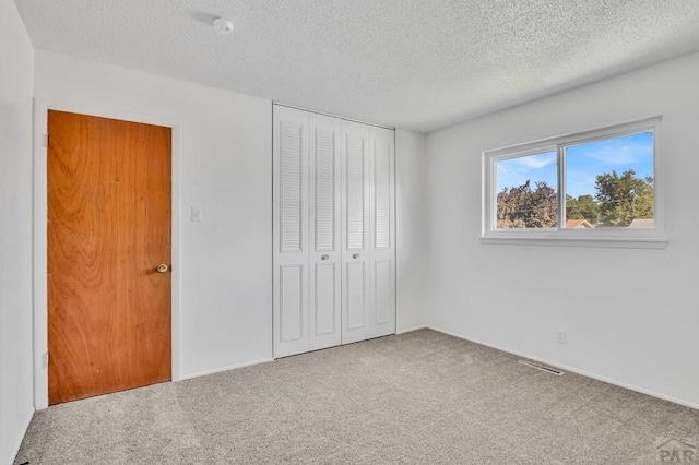 unfurnished bedroom featuring a closet, carpet, visible vents, and a textured ceiling