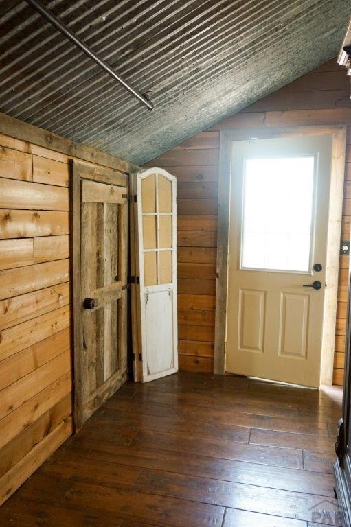 interior space featuring wood walls, vaulted ceiling, and dark wood-style flooring