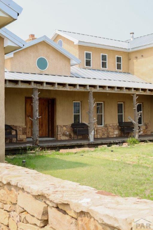 back of house with a yard, stucco siding, a standing seam roof, metal roof, and stone siding