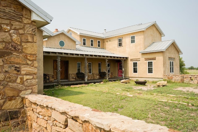 rear view of property with metal roof, a lawn, and stucco siding