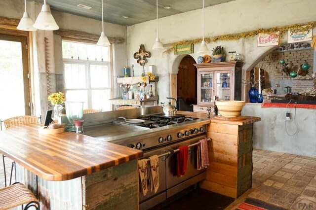 kitchen featuring arched walkways, brick floor, wood counters, double oven range, and decorative light fixtures