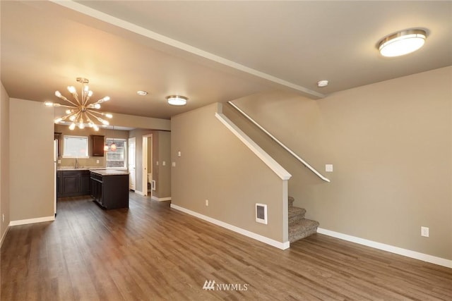 unfurnished living room with an inviting chandelier, dark hardwood / wood-style floors, and sink